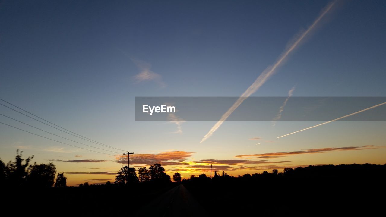 SILHOUETTE LANDSCAPE AGAINST VAPOR TRAILS IN SKY