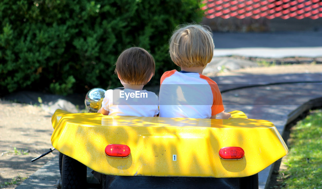 Rear view of siblings in toy car at park