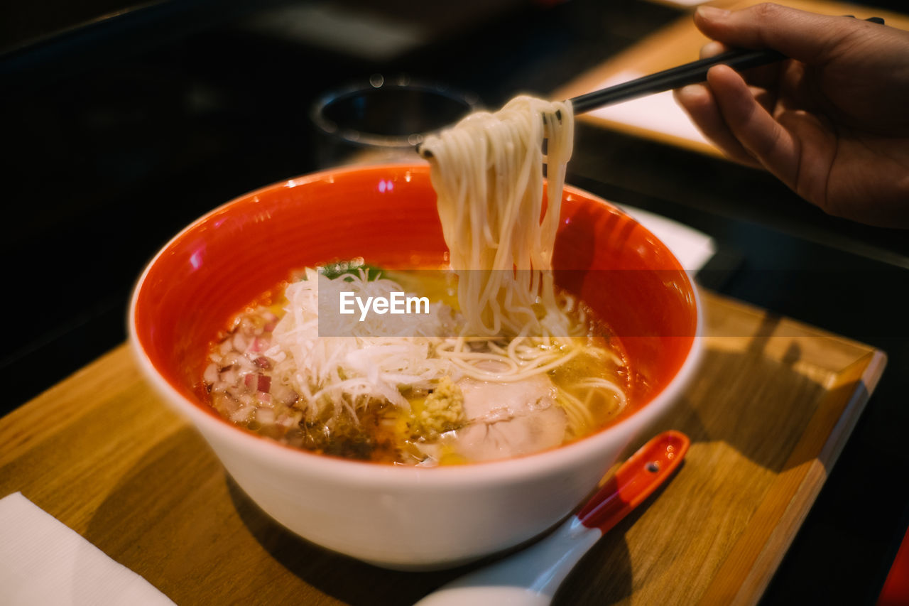 Cropped hand holding noodles in bowl on tray