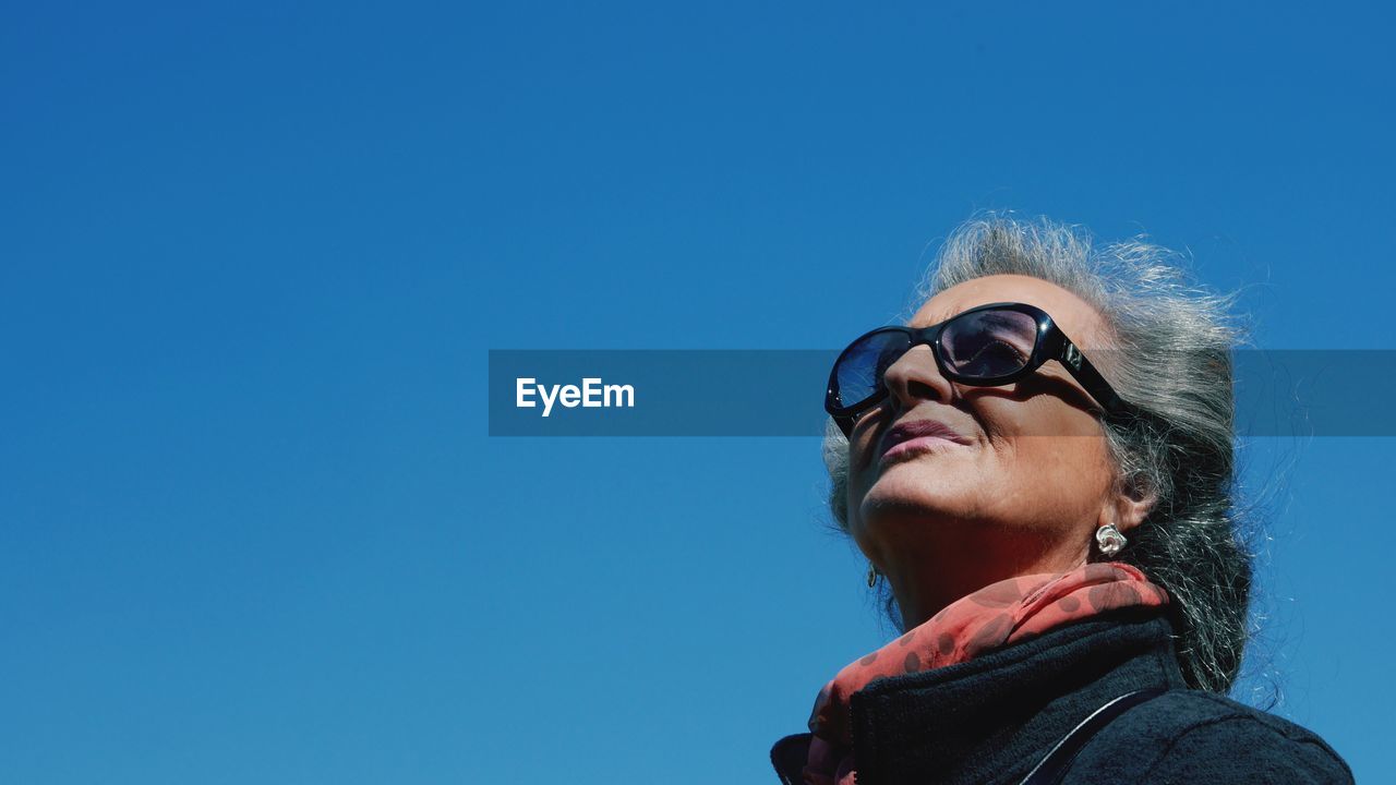 Low angle view of woman wearing sunglasses against clear blue sky