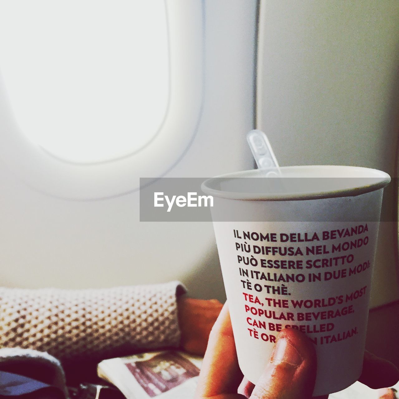 Cropped image of hand holding disposable cup with text in airplane