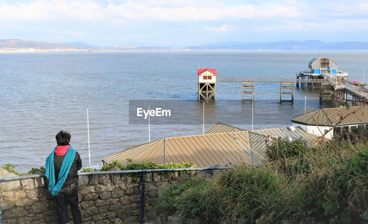 Rear view of people looking at sea and pier against sky