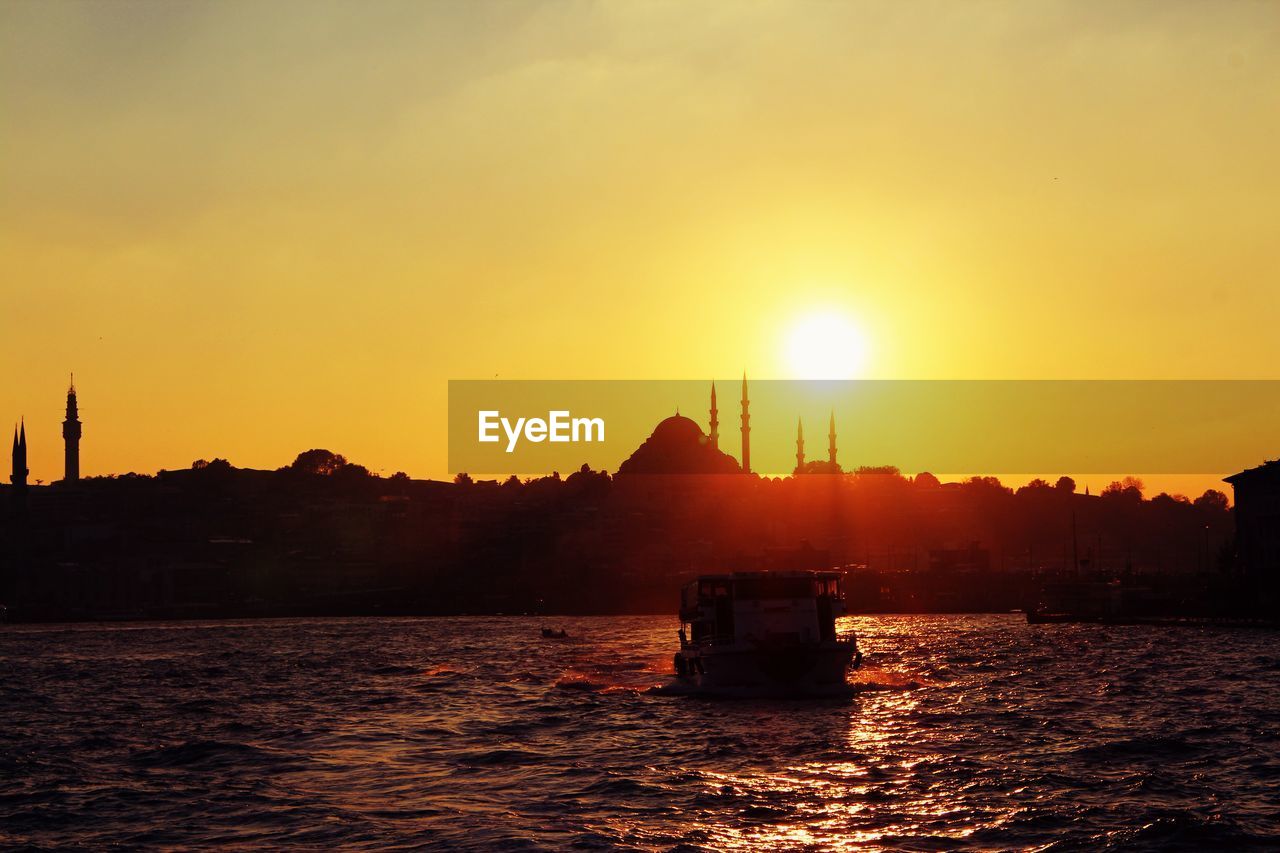 SILHOUETTE BOAT SAILING ON RIVER AGAINST ORANGE SKY