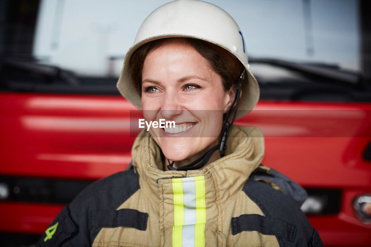 Smiling female firefighter wearing helmet looking away in fire station