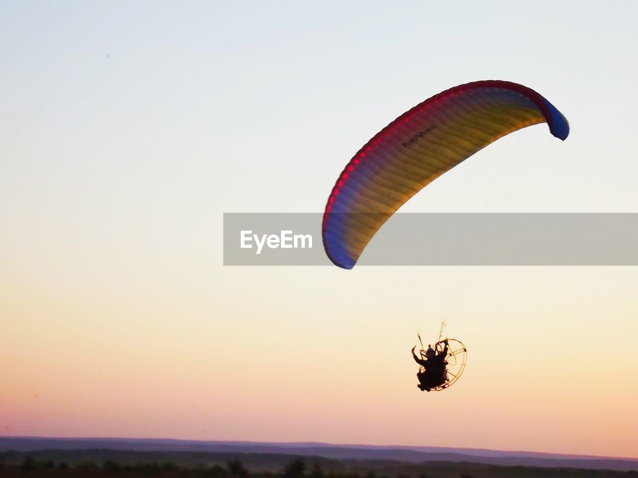 Low angle view of man flying powered parachute against clear sky during sunset