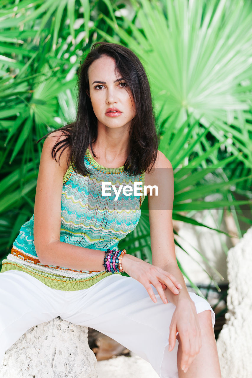 Portrait of young woman sitting against plants