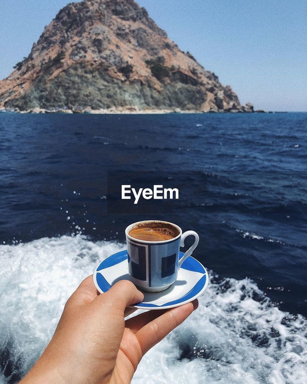 Hand holding coffee cup by sea