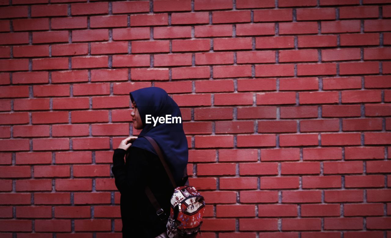 Side view of woman wearing hijab walking by brick wall