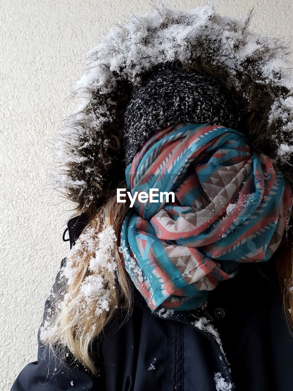 Woman with obscured face standing against wall during winter