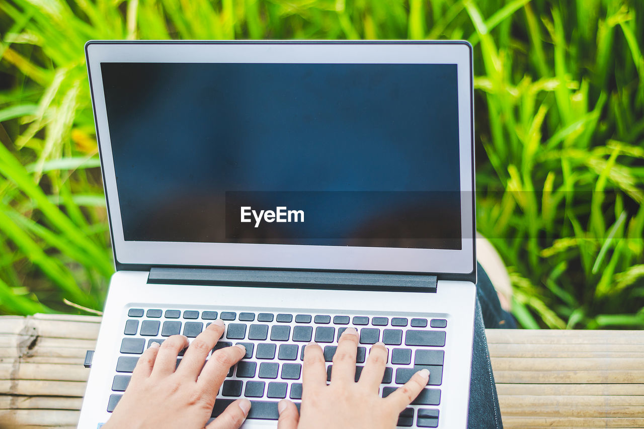 Low section of woman using laptop while sitting outdoors