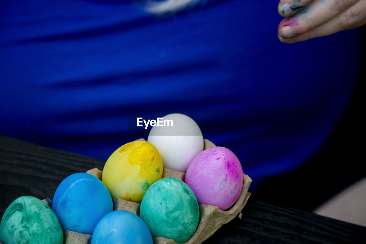 Plastic easter eggs dyed green, blue, pink, and yellow in the carton with one undyed egg
