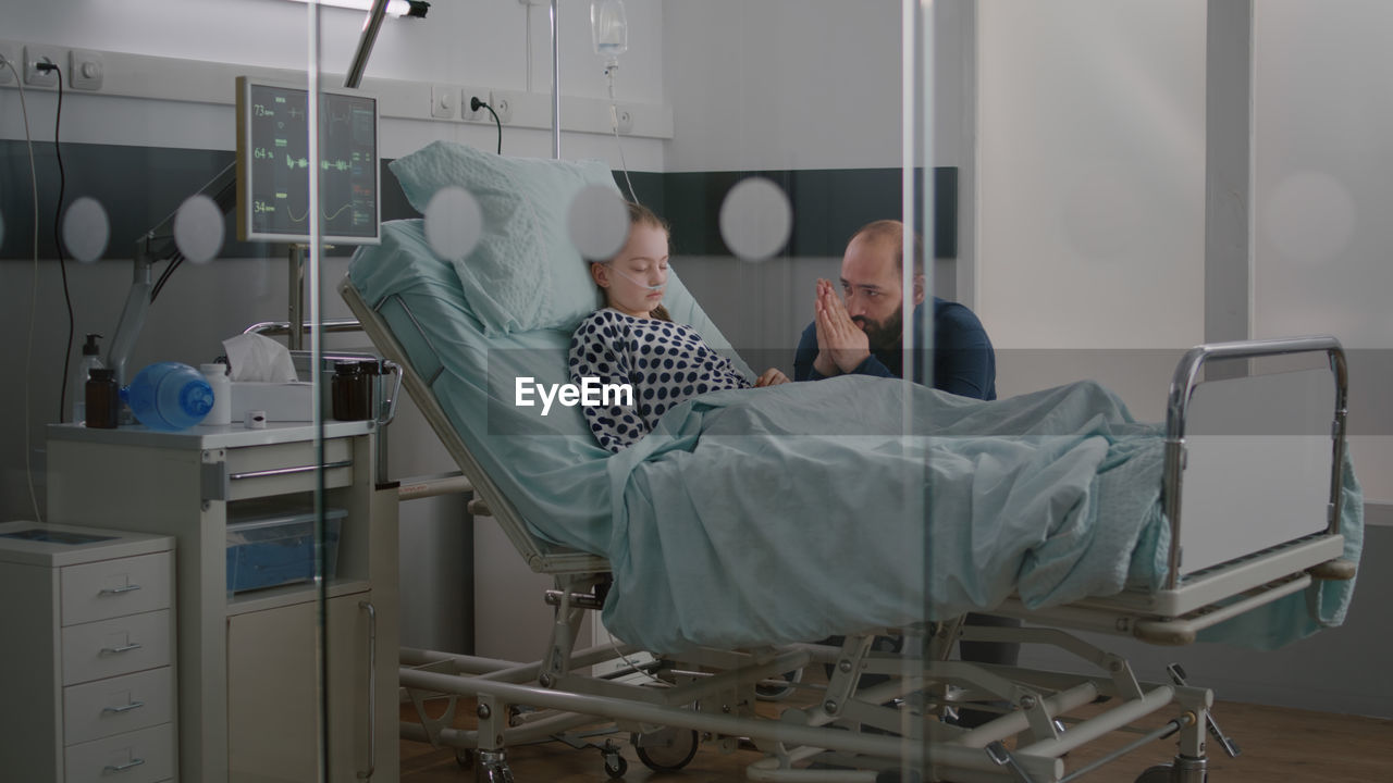 Man praying for daughter while sitting by hospital bed