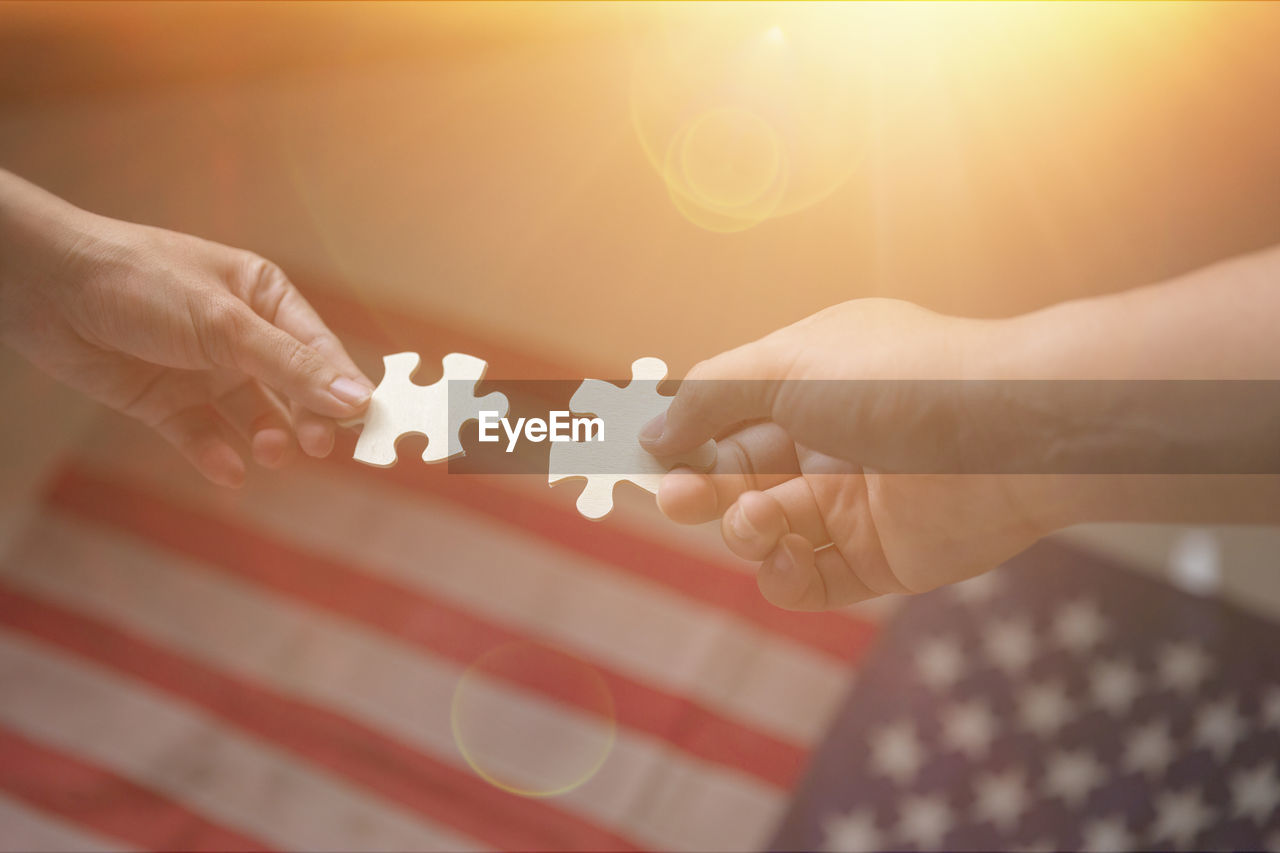 Cropped hands of people holding jigsaw pieces against american flag