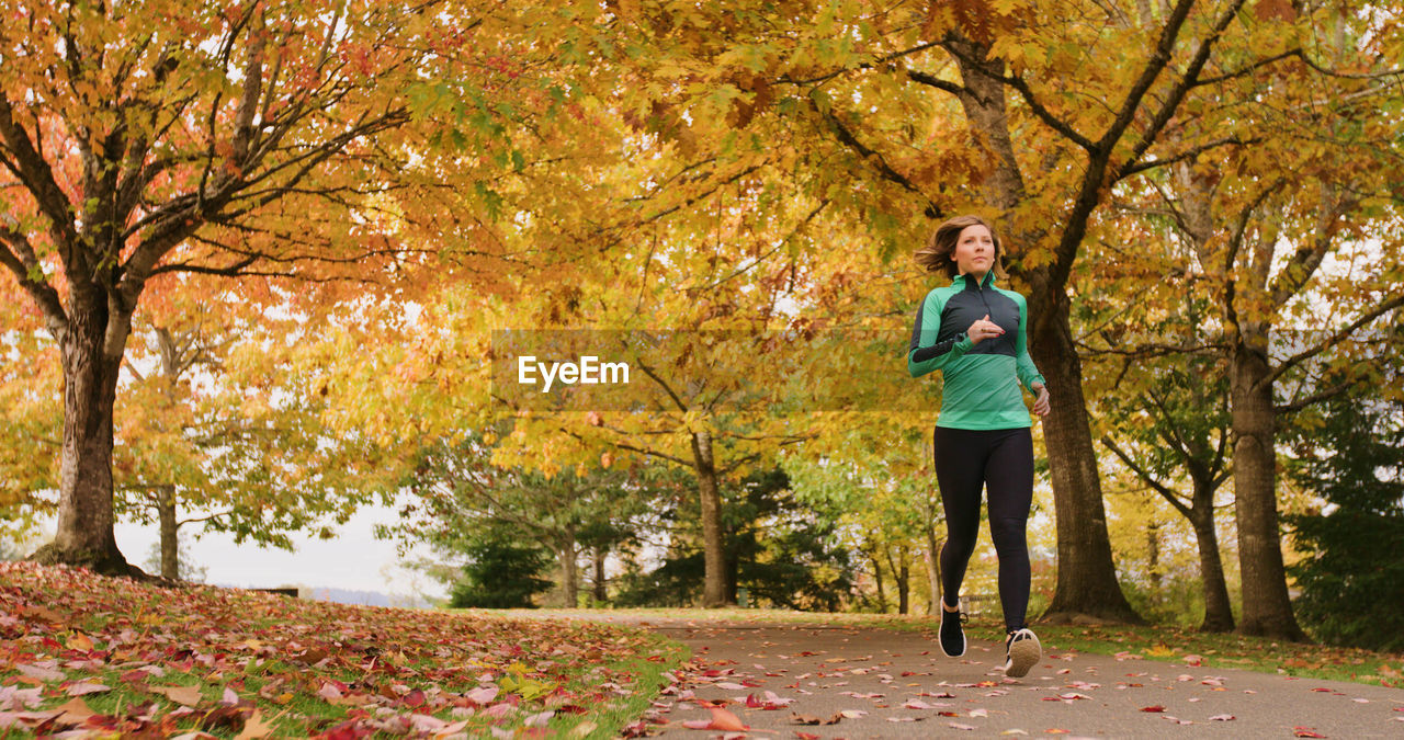 Full length of young woman jogging in park during autumn