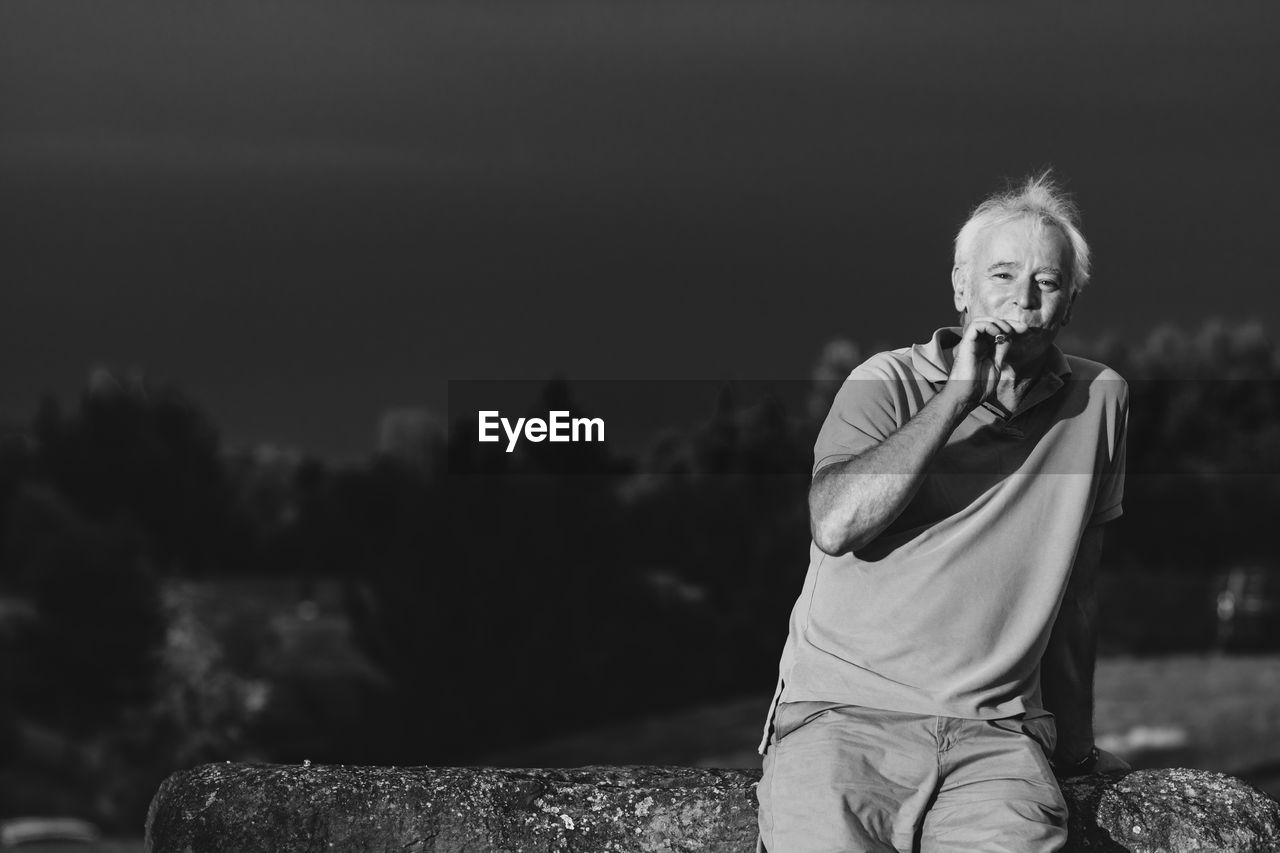 Portrait of man holding electronic cigarette while standing against trees and sky