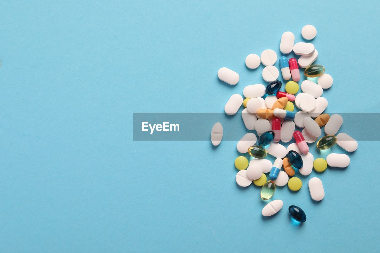 high angle view of pills spilling from bottle against blue background