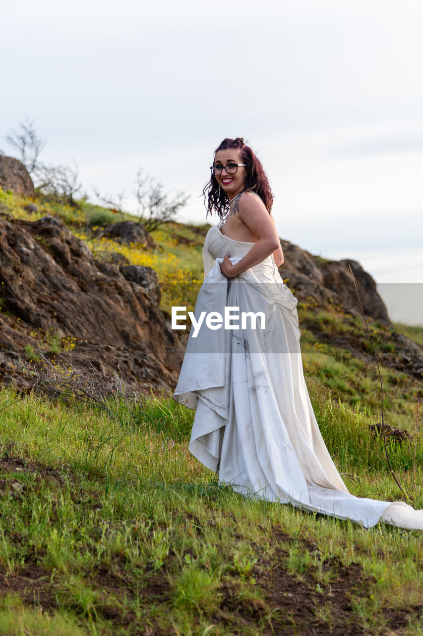 Young woman in wedding dress standing on mountain against sky