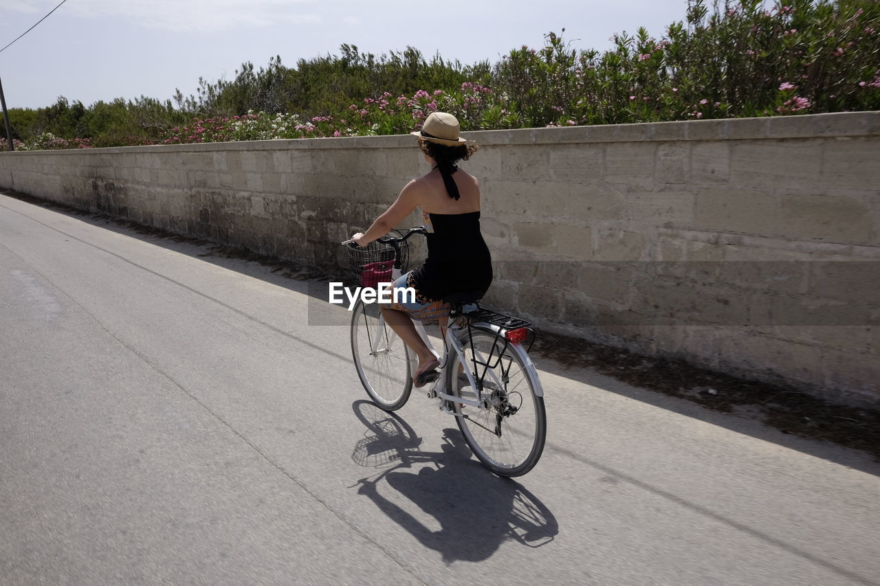 Rear view of woman cycling on road during summer