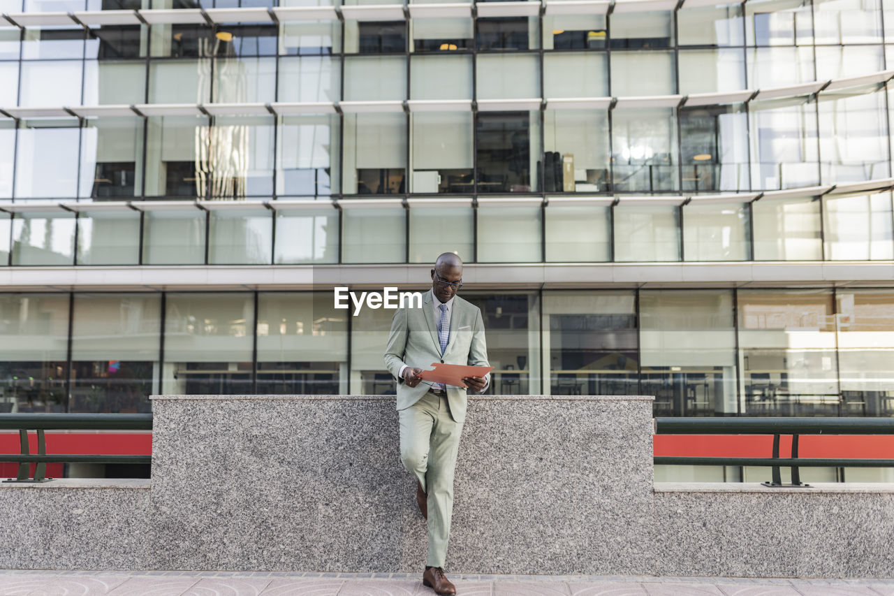 Mature businessman reading document standing in front of building