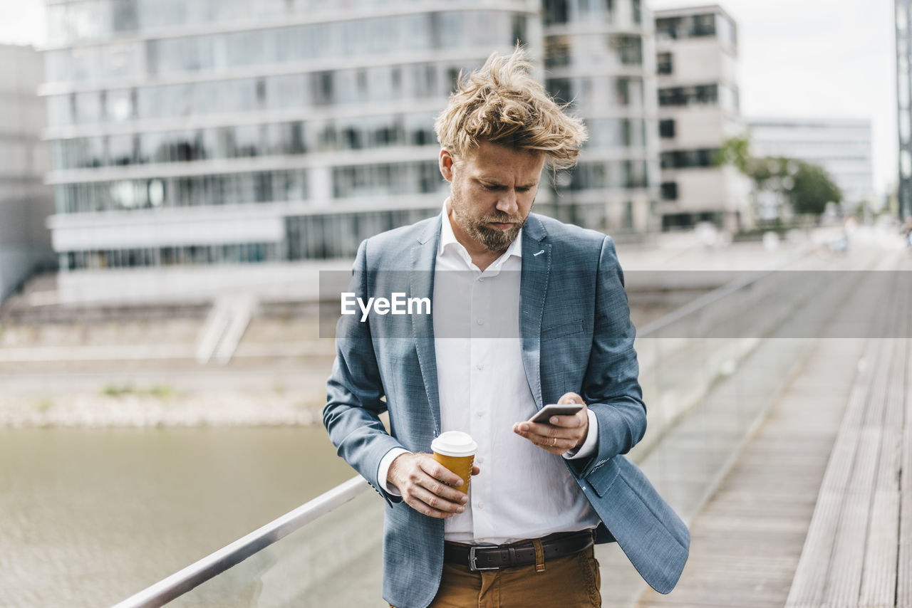 Businessman with cell phone and coffee to go on bridge