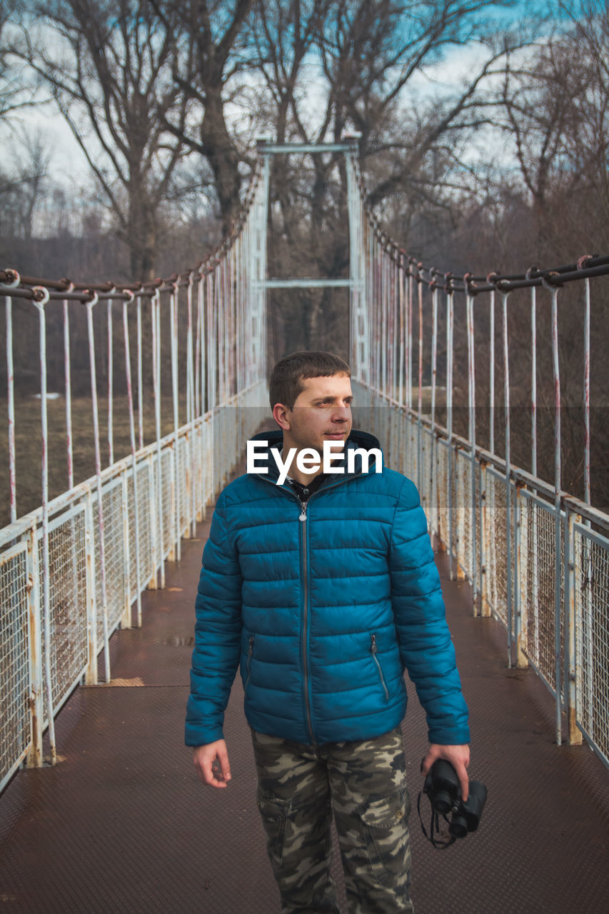 Man looking away while standing on footbridge in forest