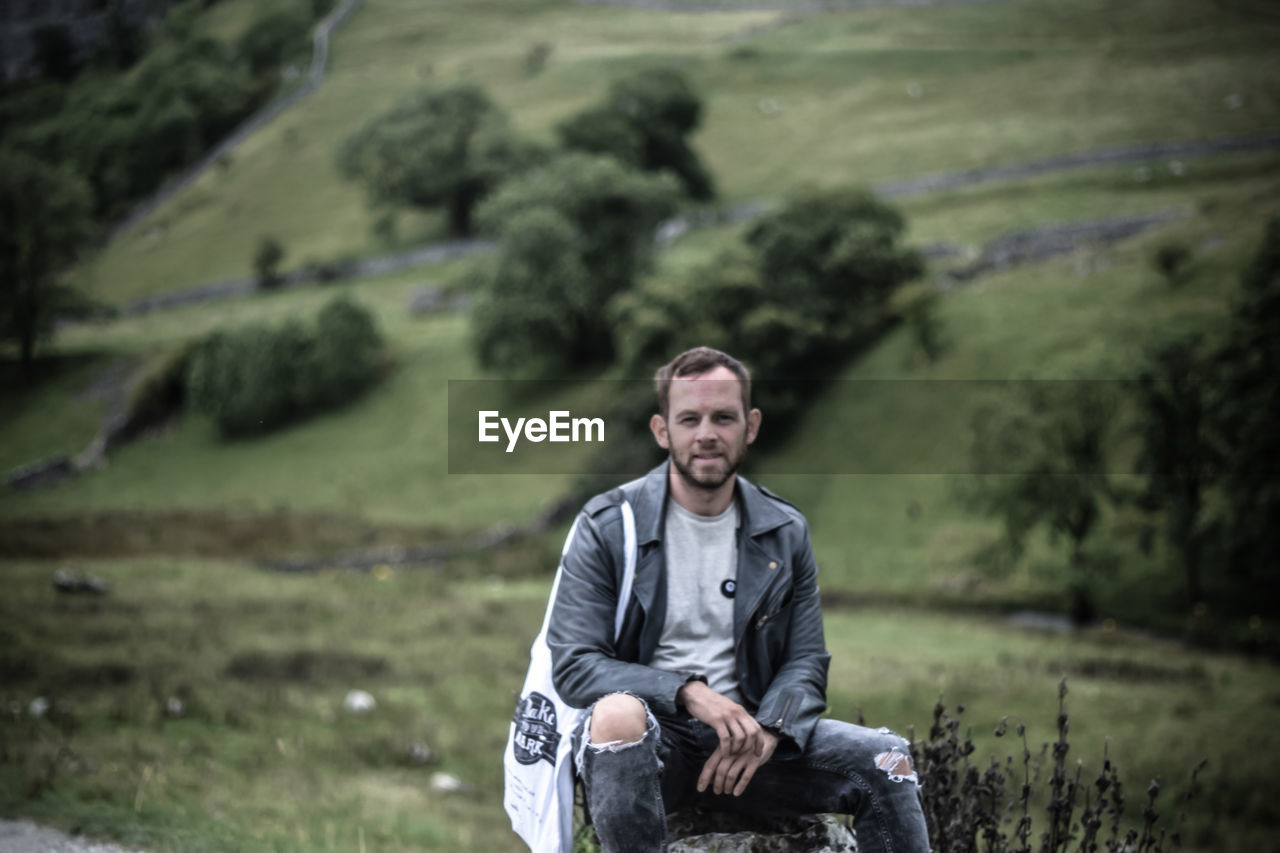 Portrait of man sitting on rock against landscape