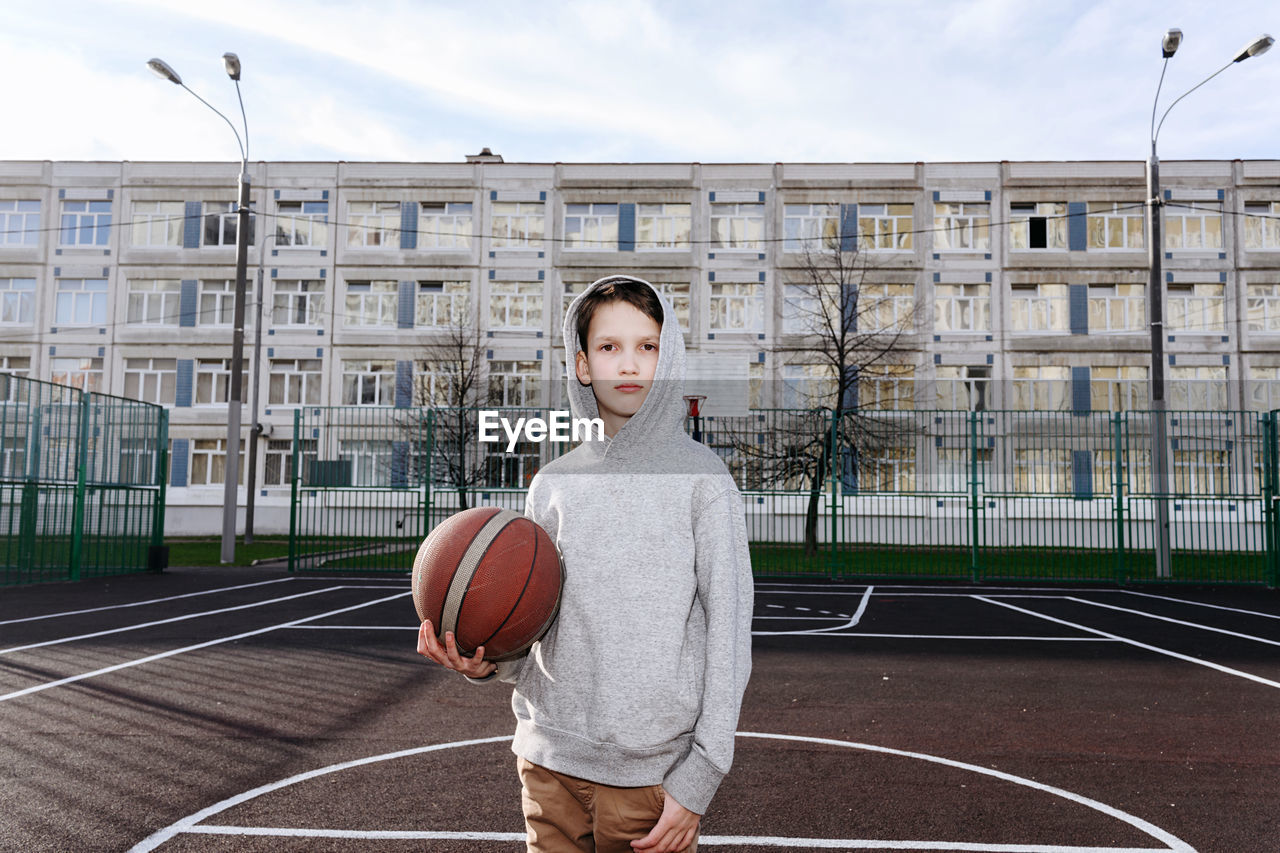 Portrait of teenager with basketball ball standing on court 