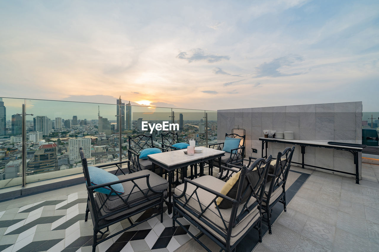 CHAIRS AND TABLE BY SWIMMING POOL AGAINST SKY