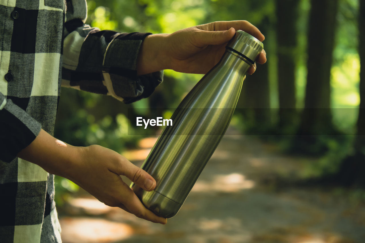 Close-up of unrecognizable female hand holding water bottle. reusable steel thermo water bottle in