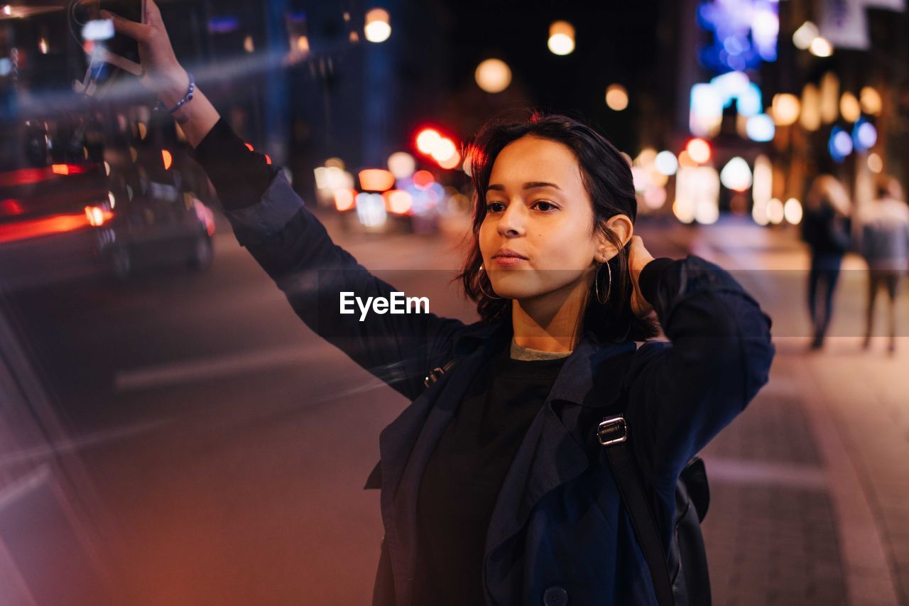 Young woman with hand in hair hailing for taxi in city at night