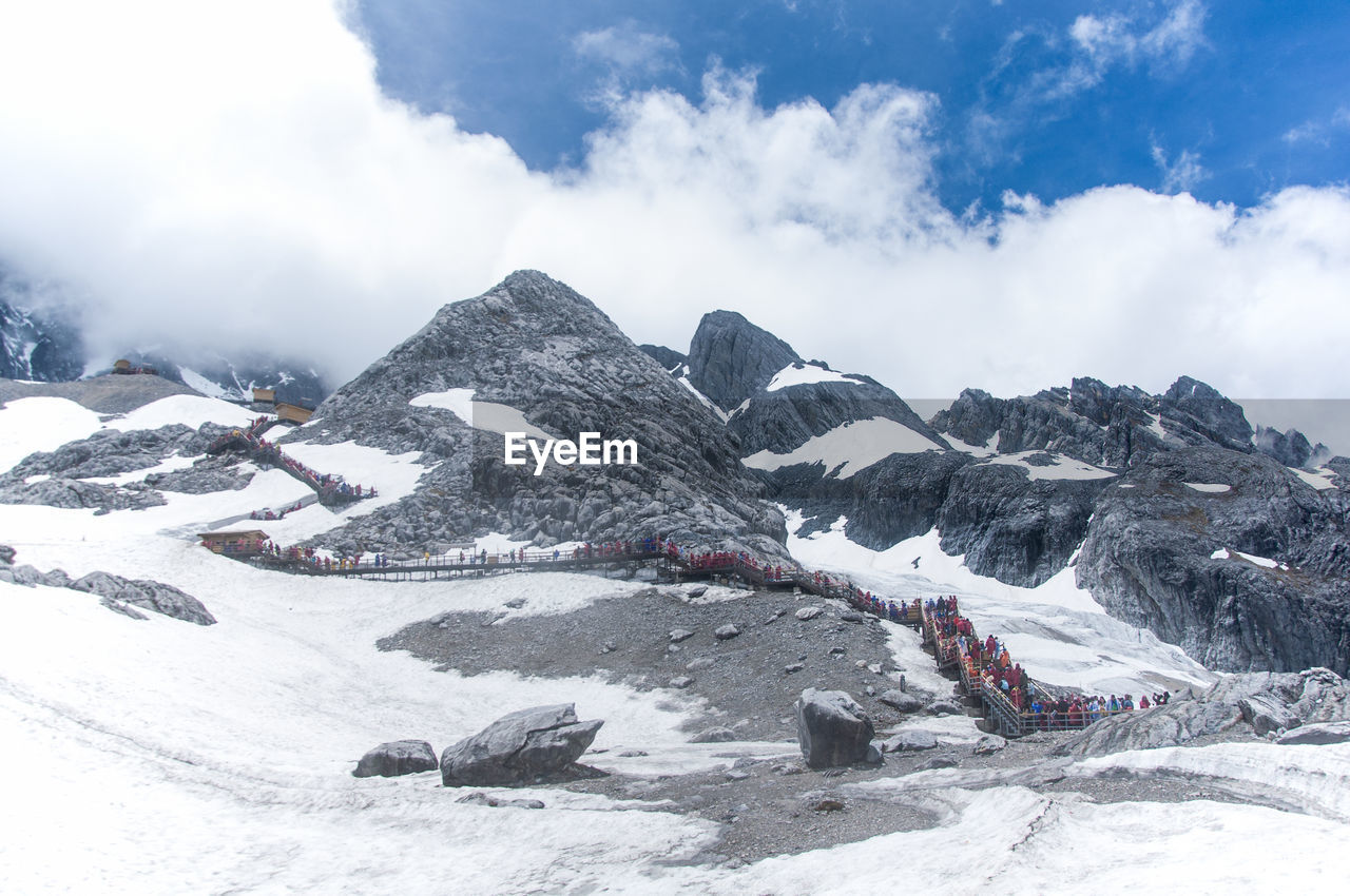 Low angle view of jade dragon snow mountains against cloudy sky on sunny day