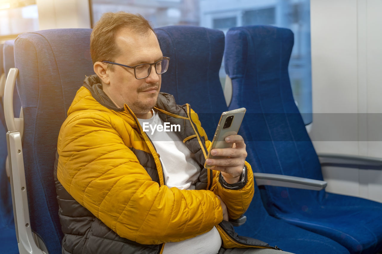 Mature man using mobile phone sitting in train