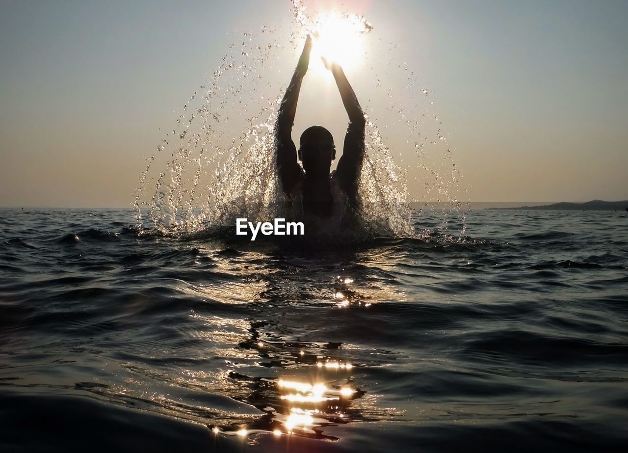 Silhouette of man splashing water in sea against sky during sunset