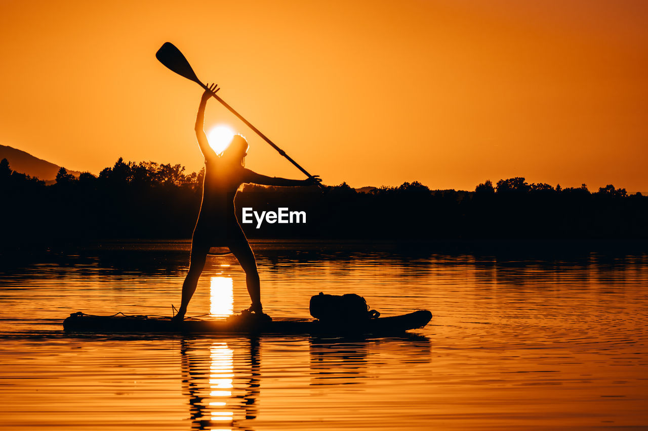 Silhouette man standing on raft against orange sky during sunset