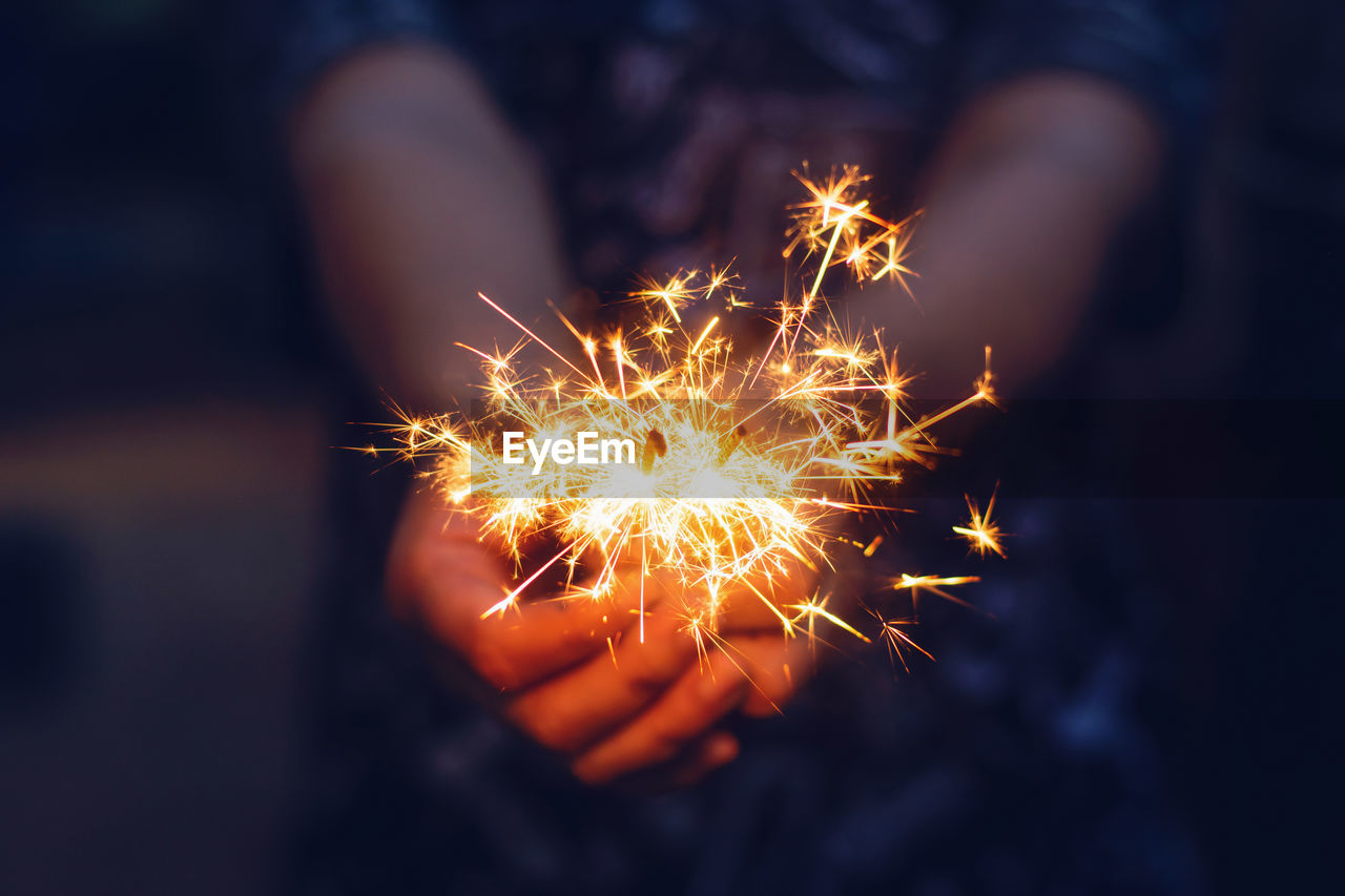 Midsection of person holding illuminated sparkler at night