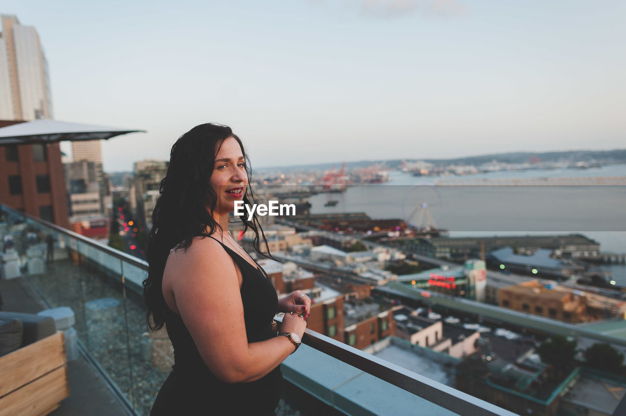 Beautiful woman standing on building terrace in city against clear sky