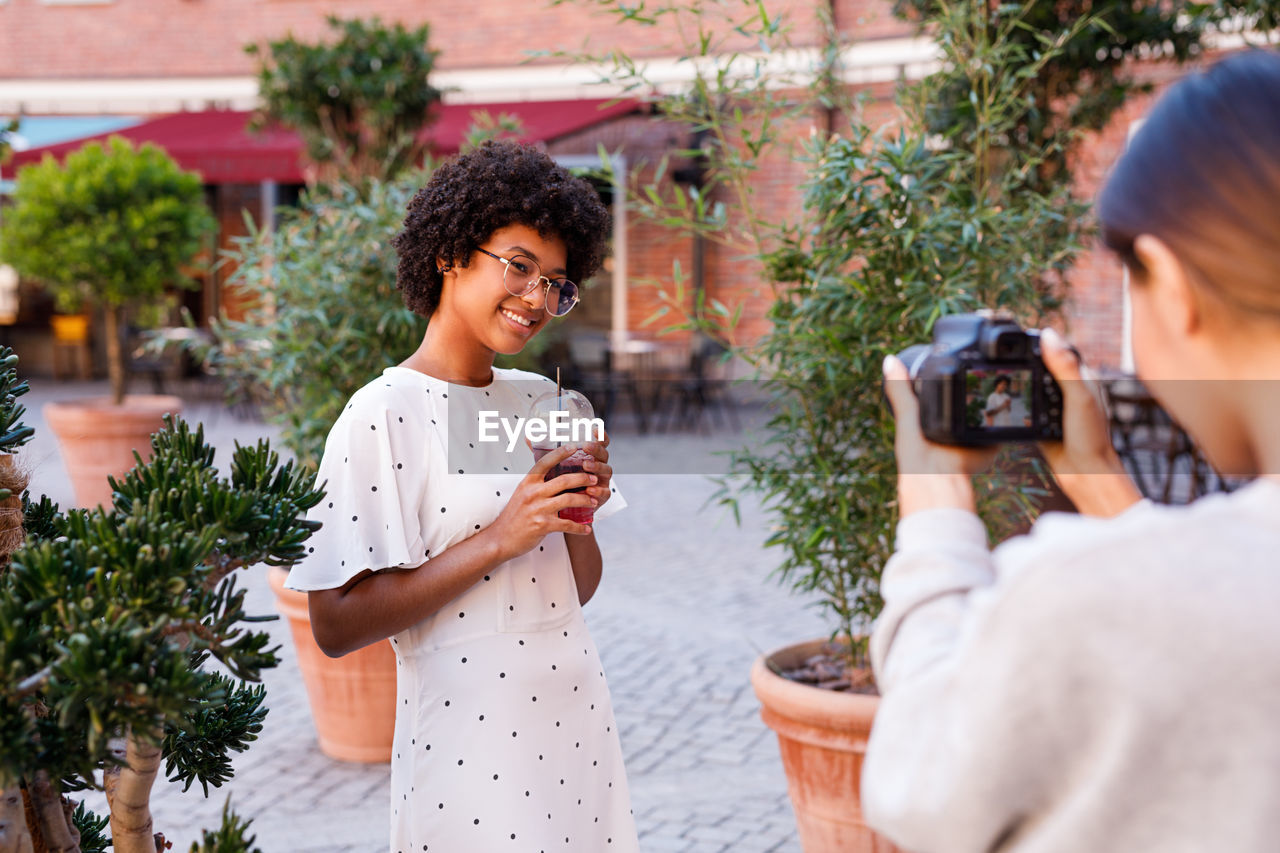 Friend photographing teenage girl through camera while standing on street