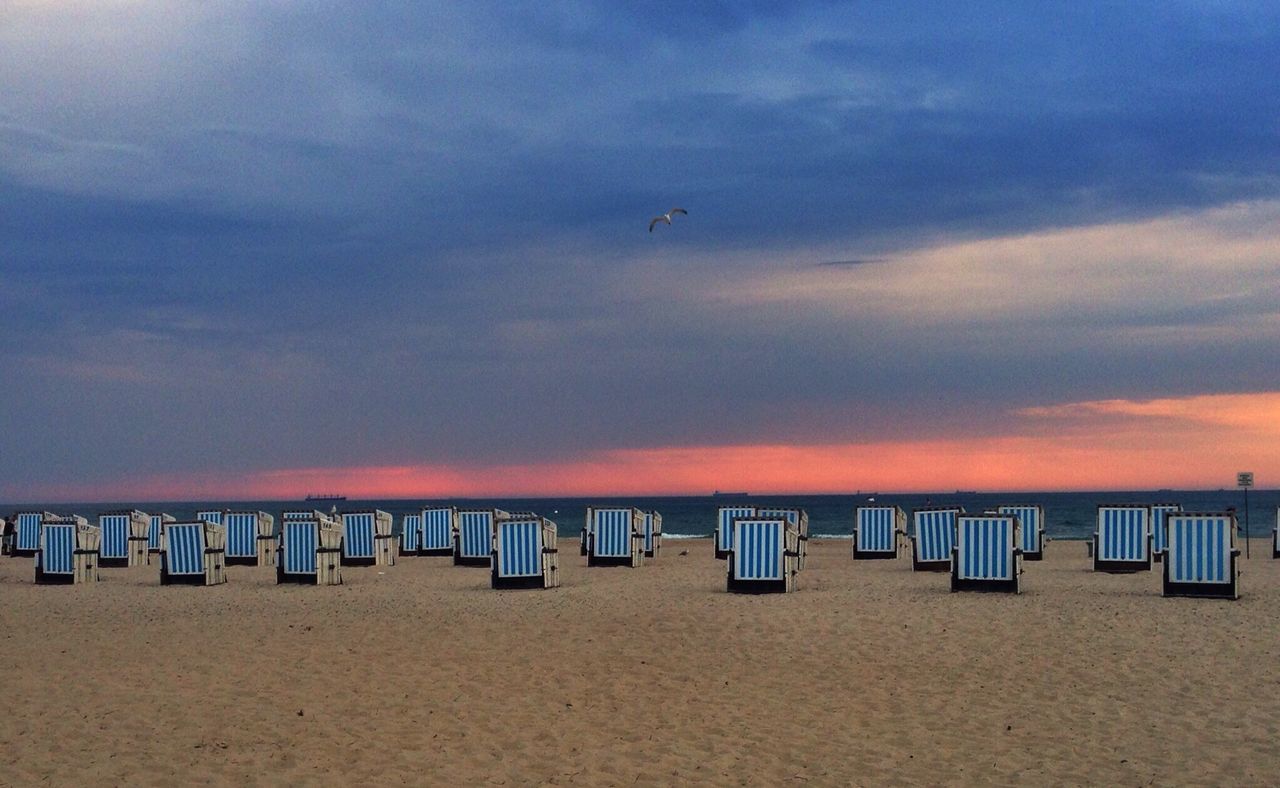 Hooded beach chairs against cloudy sky at sunset