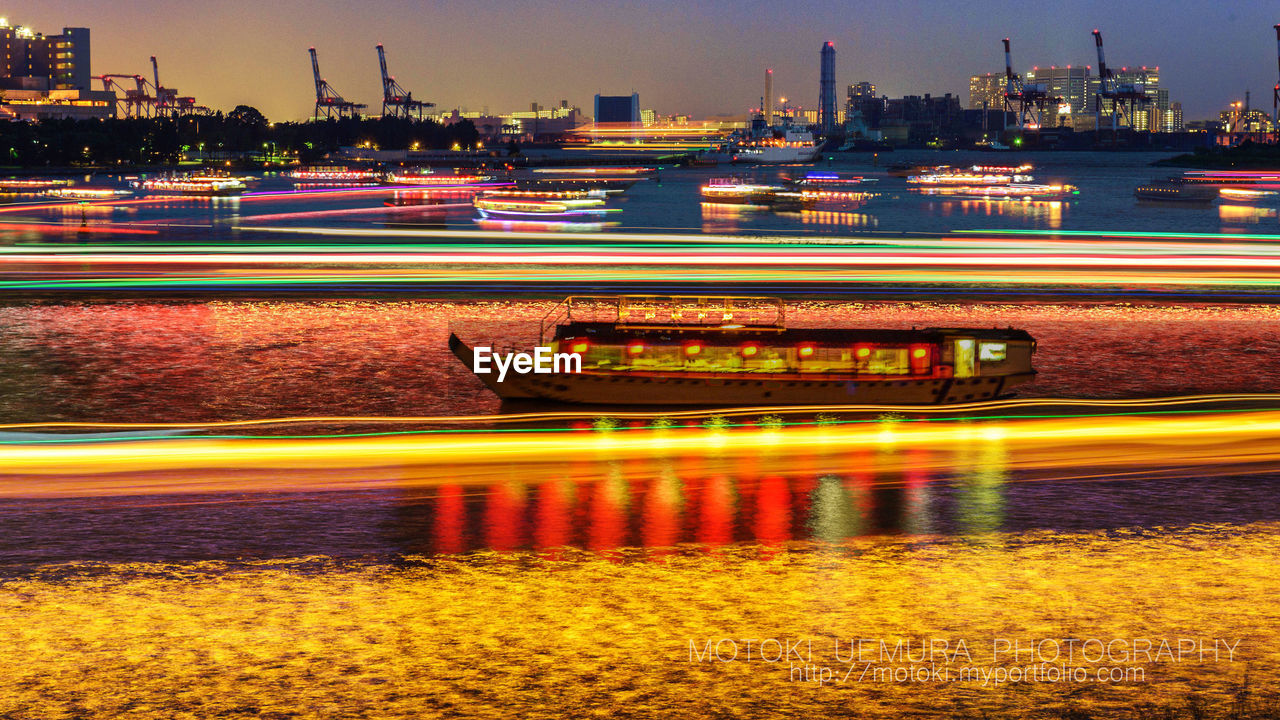 Blurred motion of illuminated bridge over river in city at night