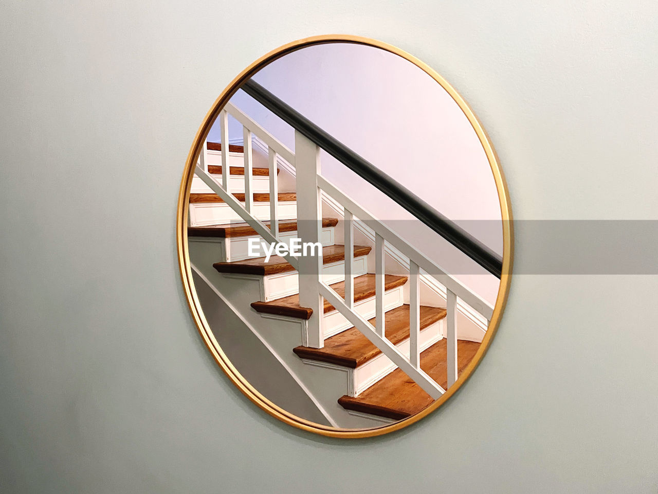 Close-up of a round mirror on a wall reflecting a wooden staircase 