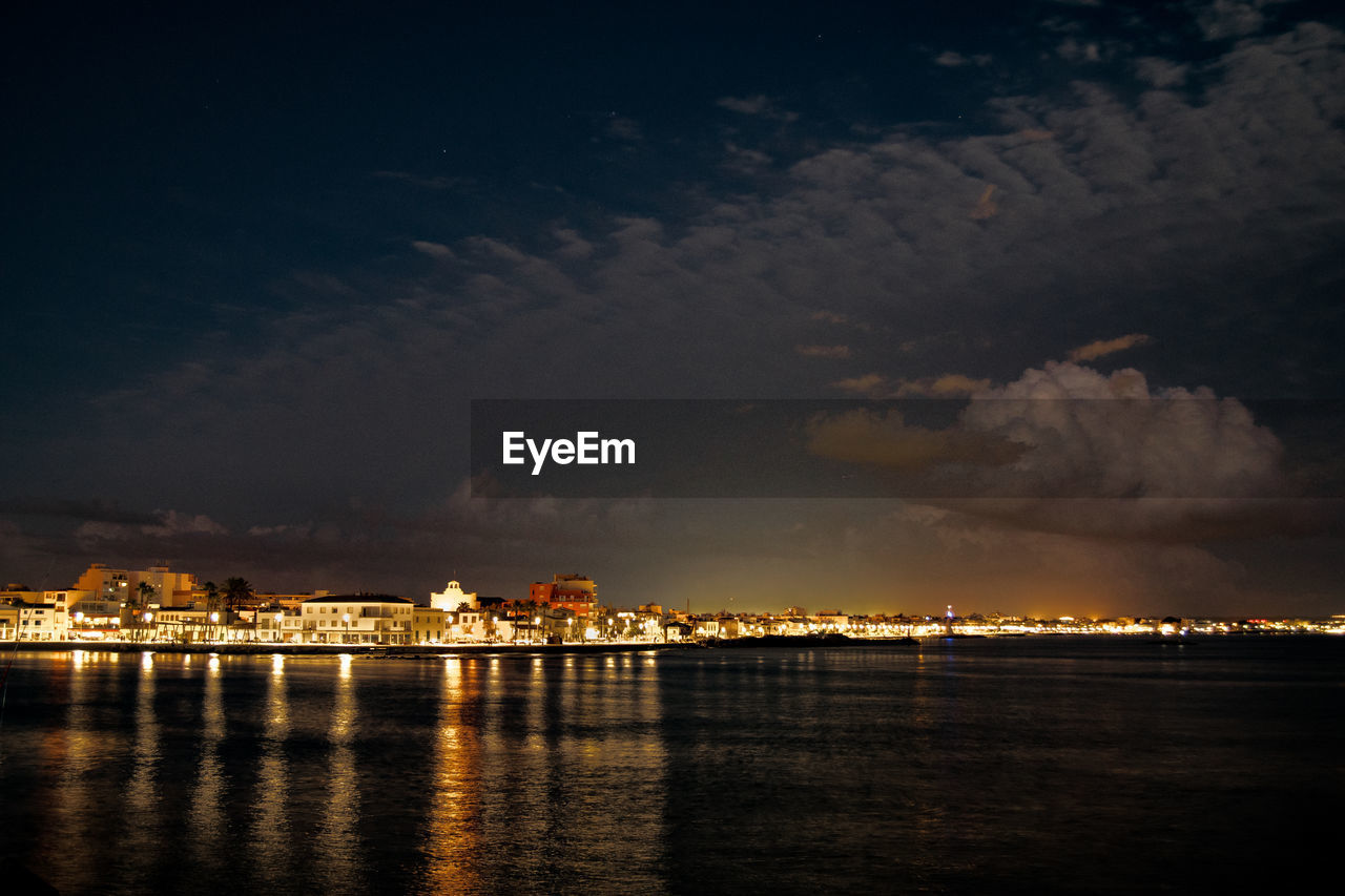 SEA BY ILLUMINATED CITY AGAINST SKY AT NIGHT