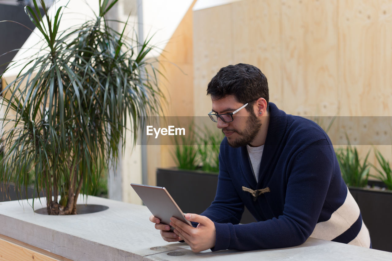 Young man reading digital tablet by plant at table