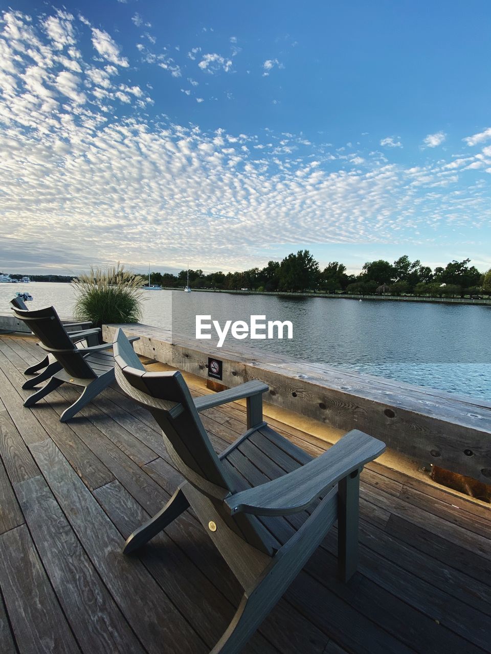 Empty chairs and table by river against sky