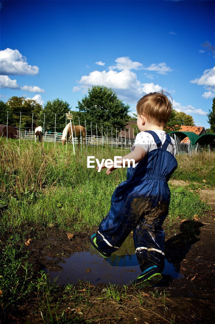 Full length of boy splashing mud on field against sky