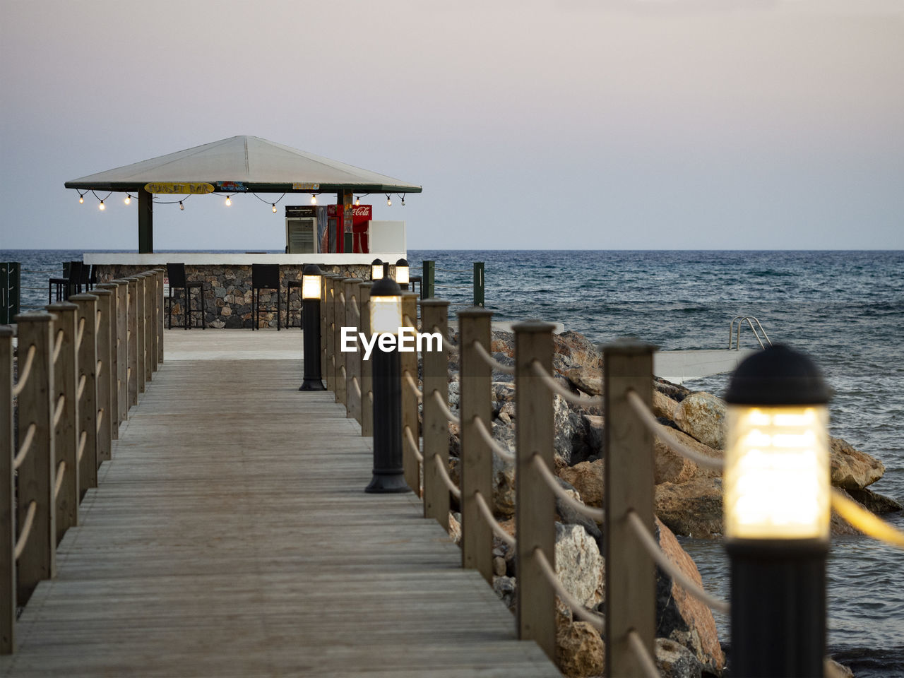 sea, water, pier, sky, horizon over water, horizon, beach, land, nature, wood, walkway, scenics - nature, ocean, tranquility, beauty in nature, boardwalk, architecture, tranquil scene, coast, railing, built structure, vacation, travel destinations, holiday, no people, idyllic, outdoors, trip, travel, clear sky, jetty, the way forward, day, hut, shore, tourism, sunset, seascape, dock, protection, breakwater, security, non-urban scene, footpath, sand, transportation, sunlight