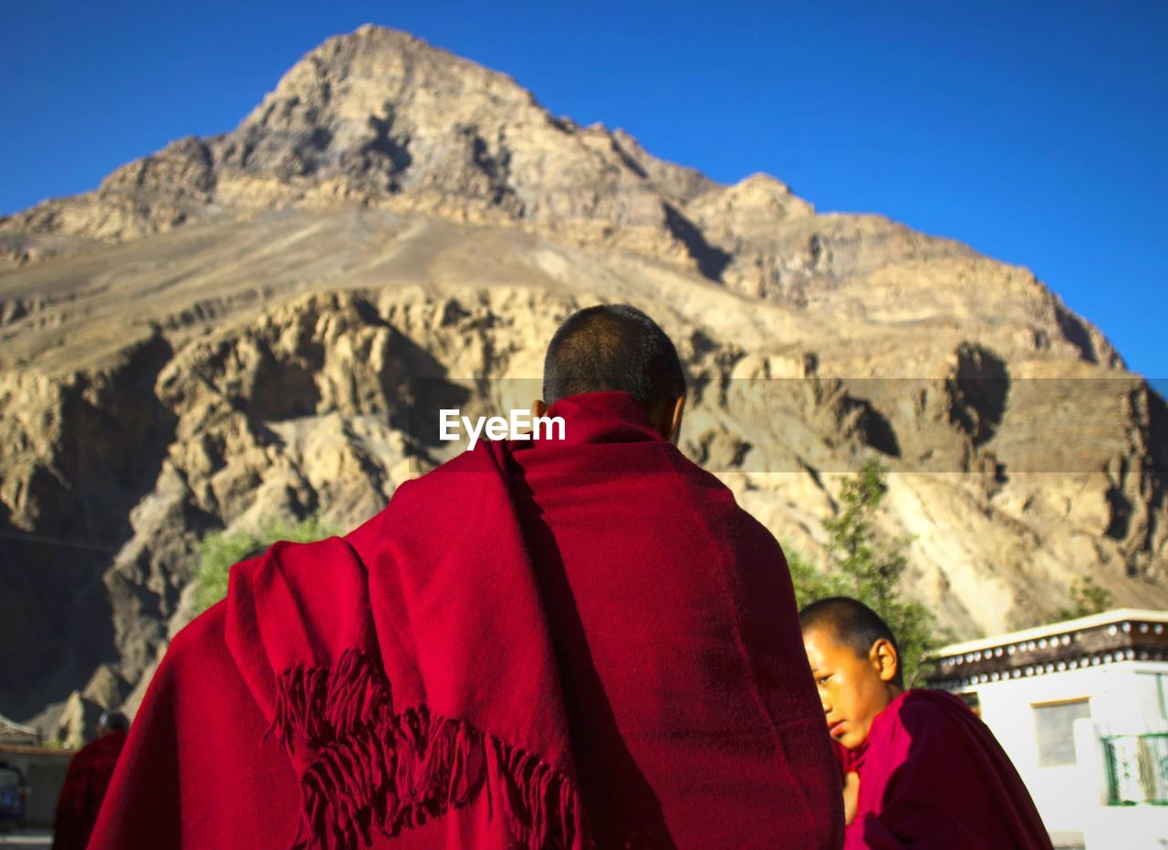 REAR VIEW OF MAN AND WOMAN ON ROCK AGAINST MOUNTAIN