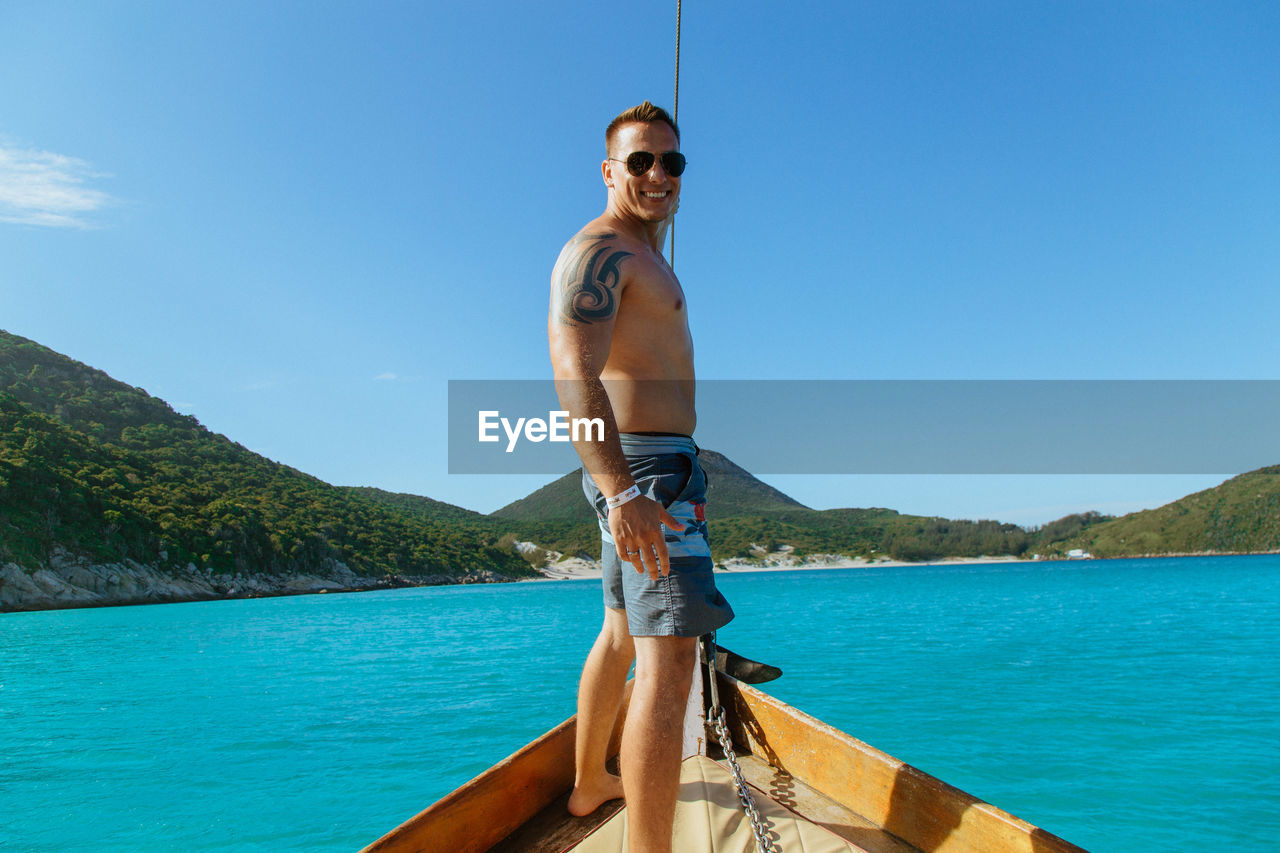 Portrait of man standing in boat on sea against sky