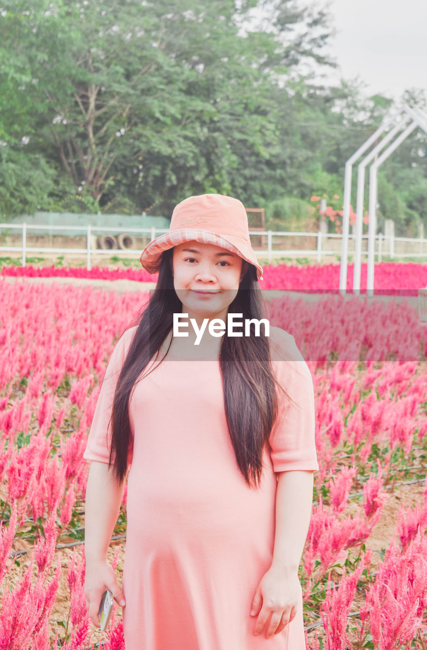 pink, plant, one person, flower, flowering plant, women, smiling, portrait, long hair, clothing, nature, adult, young adult, looking at camera, happiness, hat, standing, hairstyle, beauty in nature, emotion, front view, three quarter length, day, dress, spring, field, fashion, lifestyles, red, freshness, growth, outdoors, leisure activity, waist up, brown hair, summer, cheerful, rural scene, tree, agriculture, teeth, smile, land, teenager, landscape, springtime, child, enjoyment, casual clothing, female