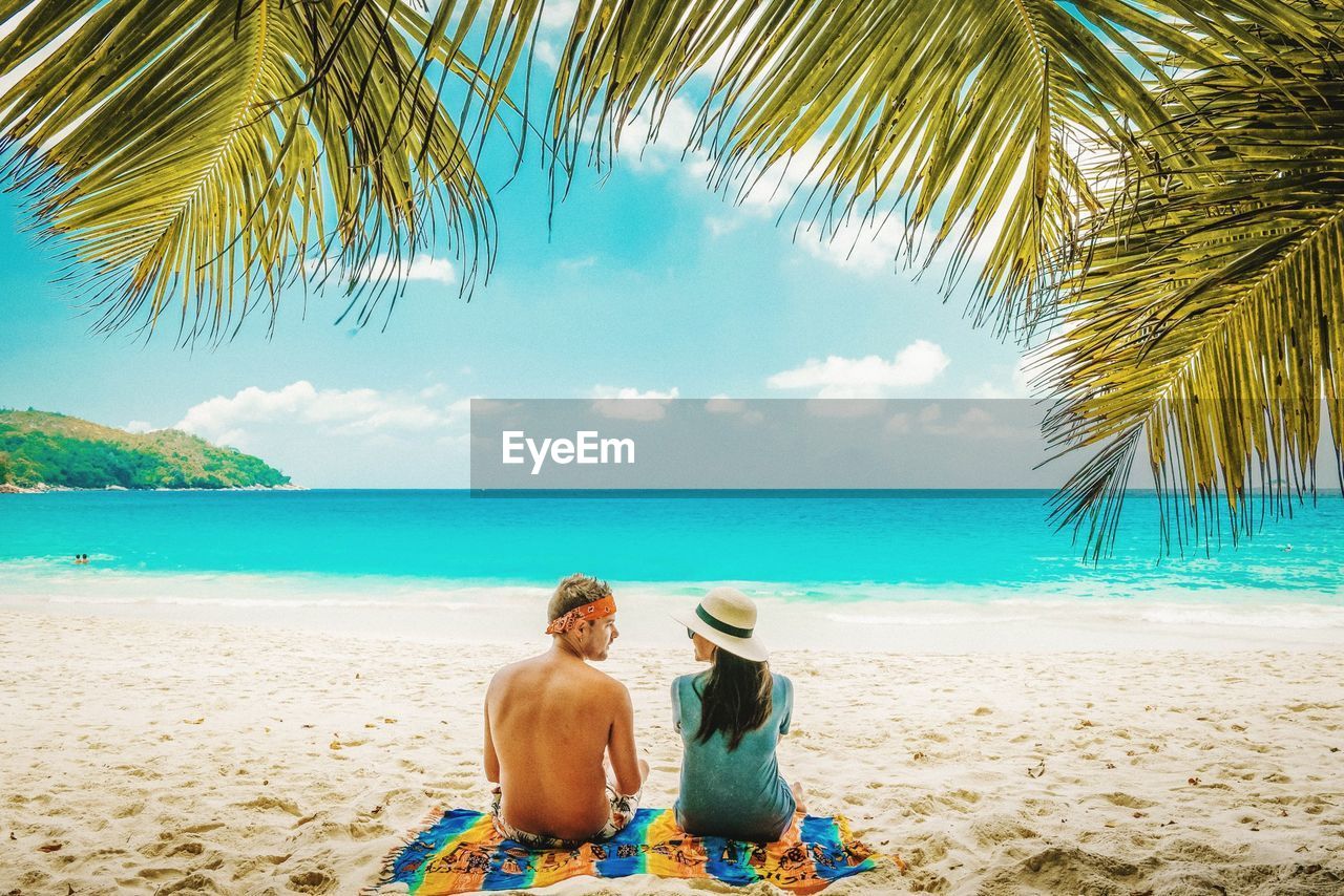 Rear view of couple sitting at sandy beach