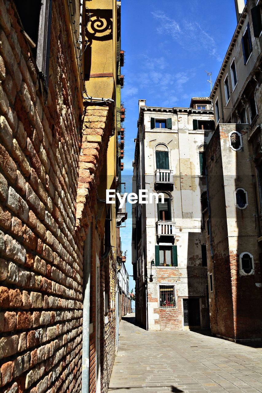 NARROW ALLEY AMIDST OLD BUILDINGS AGAINST SKY